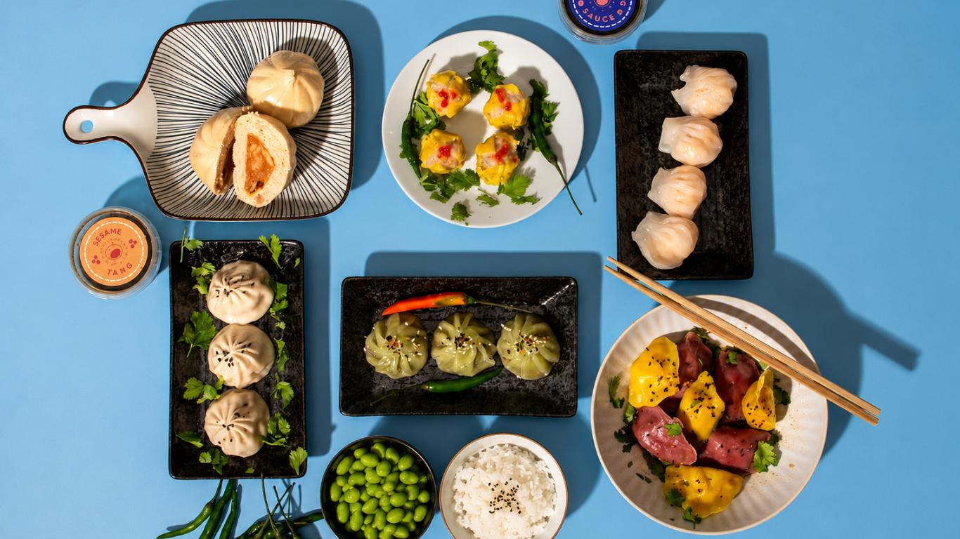Assorted Japanese dishes including dumplings sui mai, bao buns and vegetables on a blue background