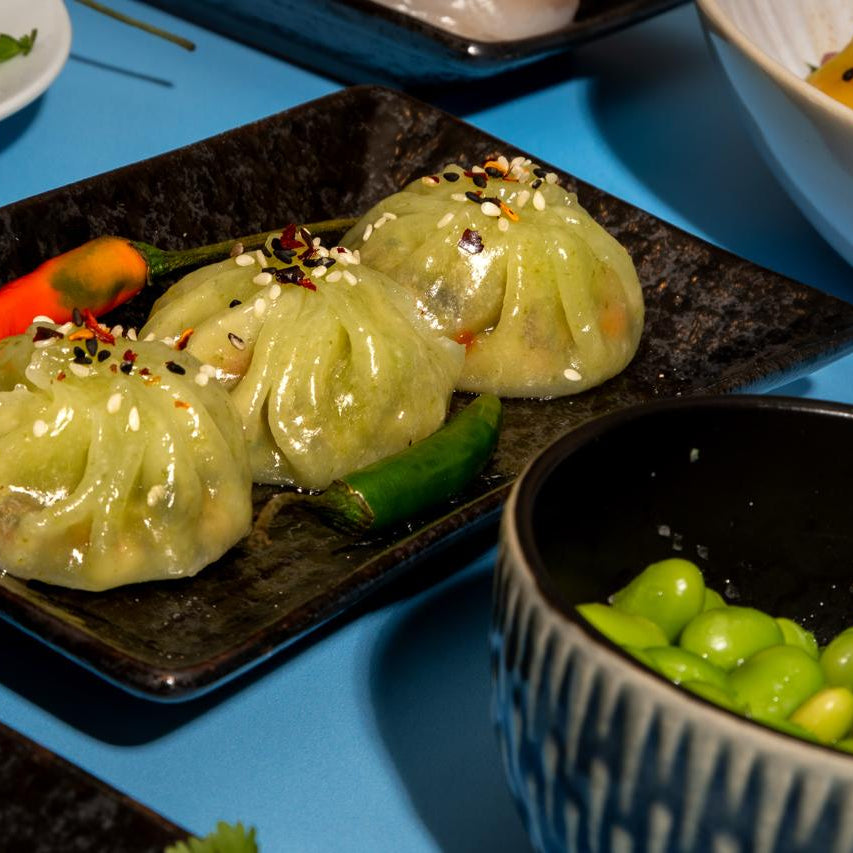 Three green dumplings on a black plate with a blue background