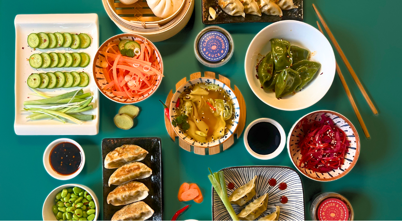 Assorted Asian dishes including dumplings, wonton soup, gyoza, salads, and pickled vegetables on a teal background